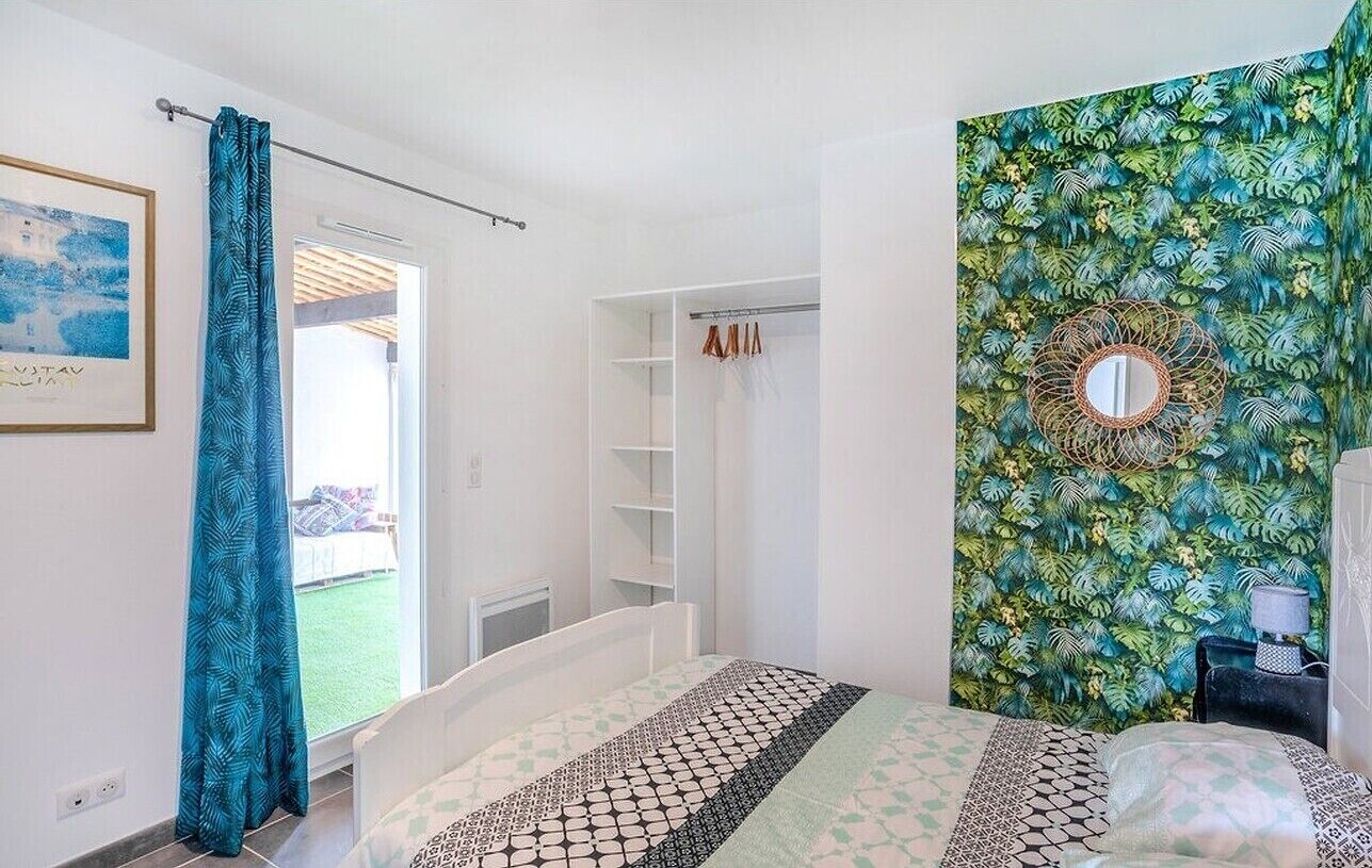 Une chambre à coucher avec un lit, une armoire, un miroir et un papier peint aux motifs tropicaux.