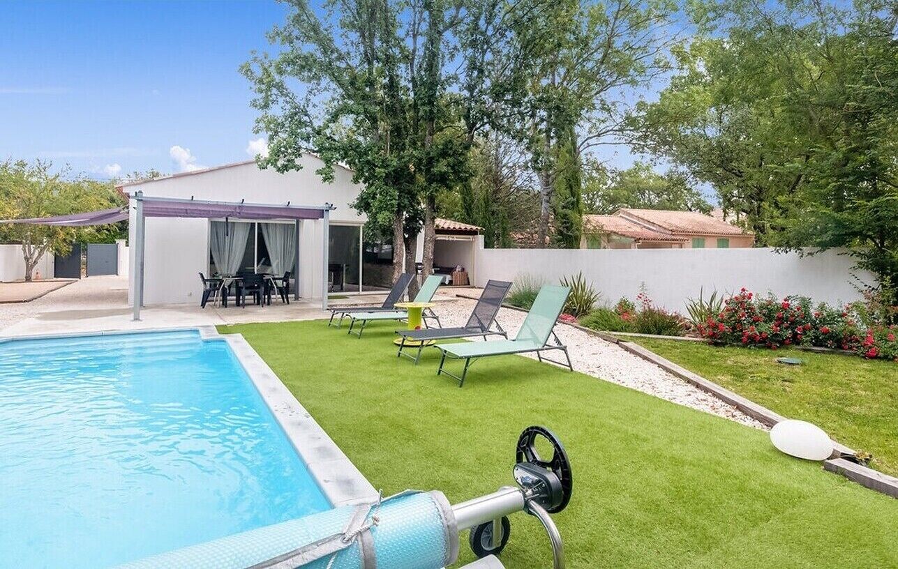 A backyard with a swimming pool, a covered patio, and outdoor seating.