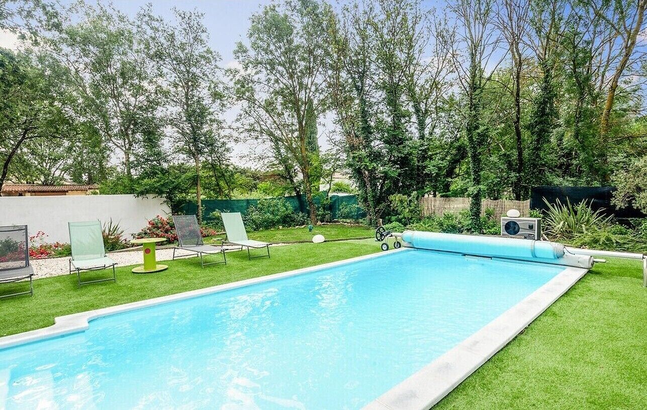 Une piscine bordée d’une pelouse verdoyante, quelques chaises longues et une petite table.