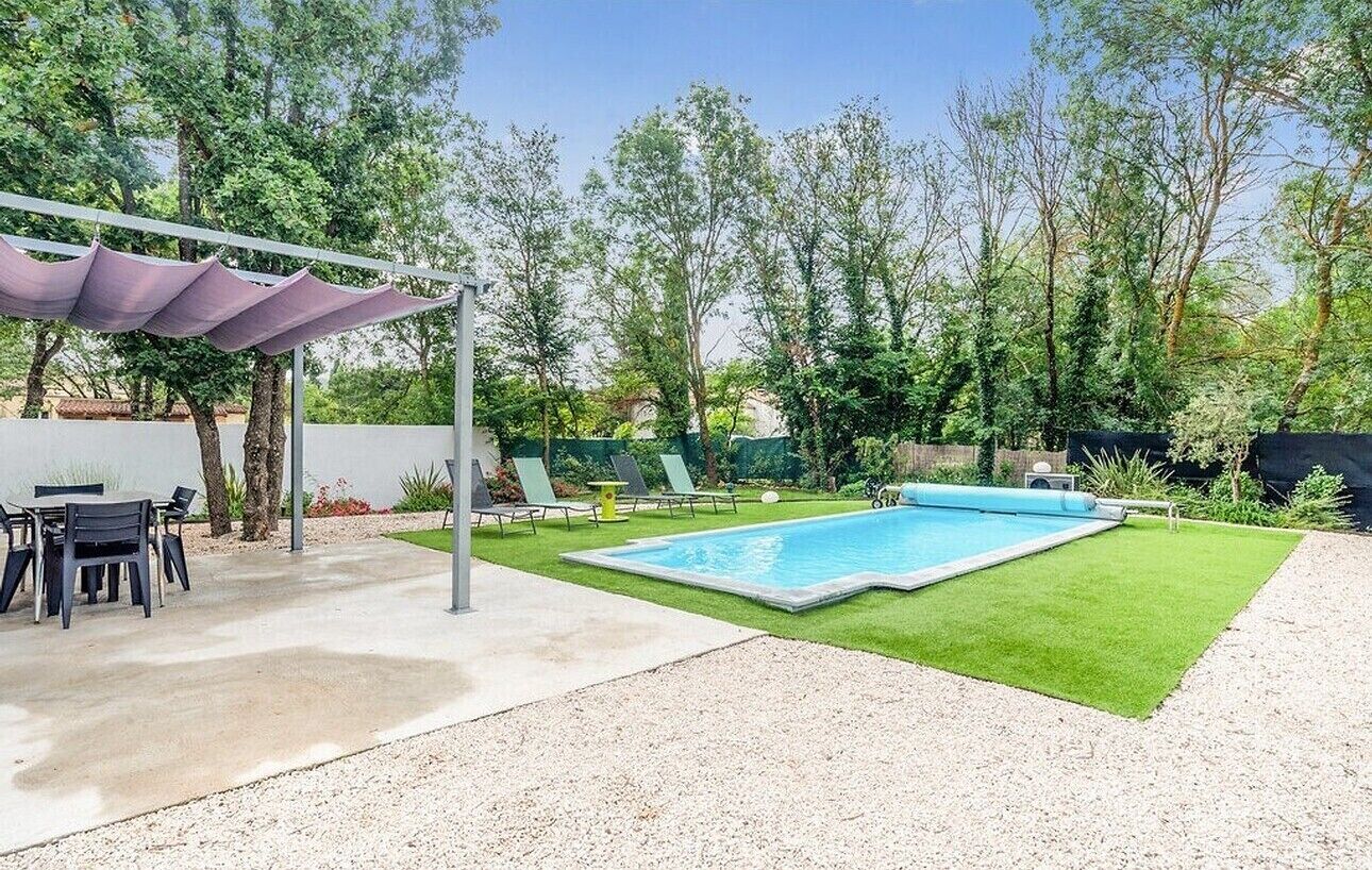 A backyard with a swimming pool, a covered patio area, and a lawn.