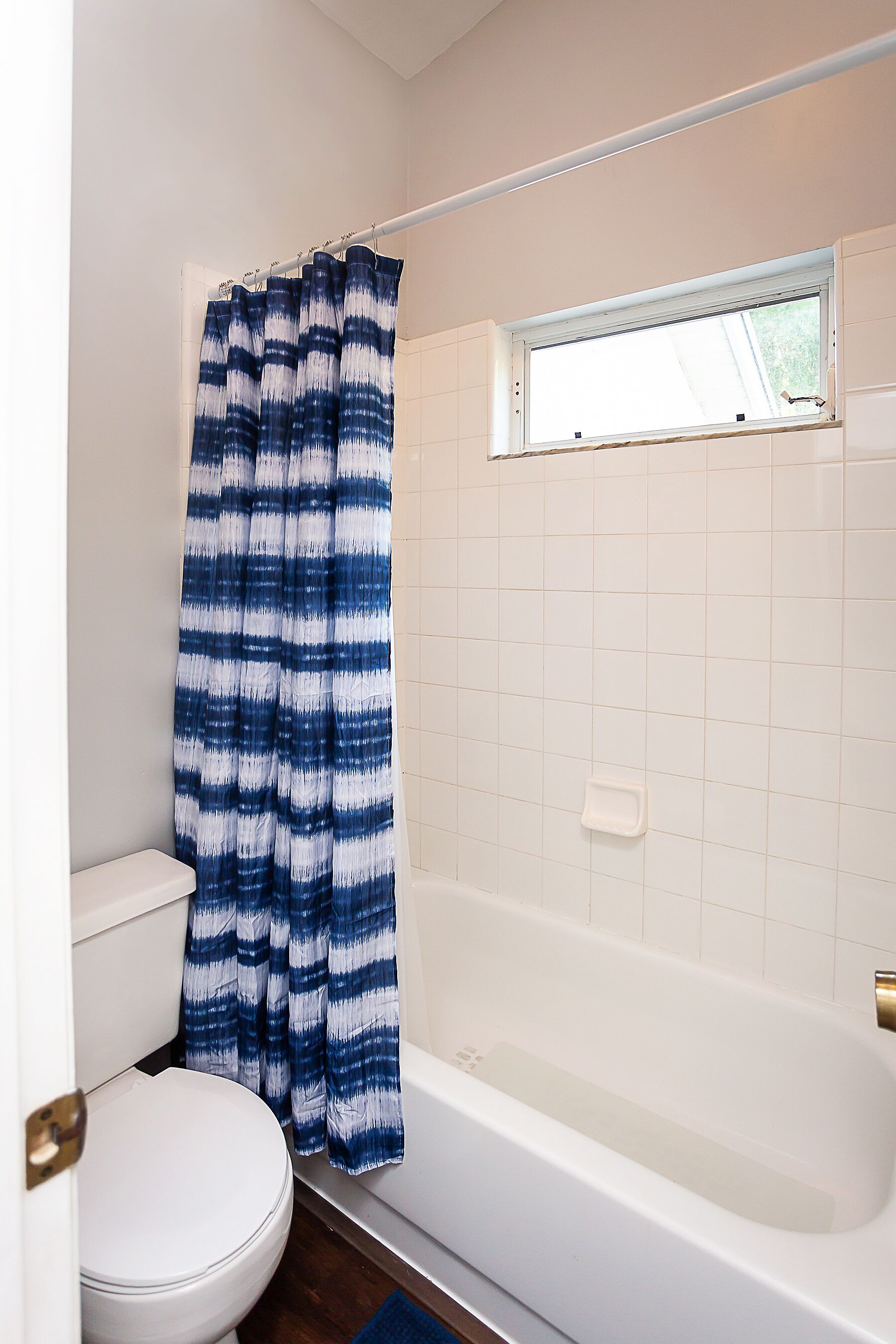 Ein Badezimmer mit einer weißen Toilette, einer weißen Badewanne und einem blauen und weißen Streifen-Duschvorhang.