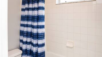 Ein Badezimmer mit einer weißen Toilette, einer weißen Badewanne und einem blauen und weißen Streifen-Duschvorhang.