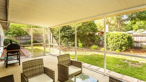 Ein überdachter Patio-Bereich mit Korbmöbeln und einer Glastür, die in einen Garten führt.