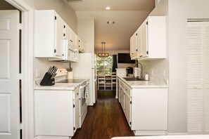 A narrow kitchen with white cabinets and a wooden floor.