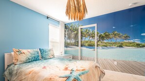 Une chambre avec un grand lit, une vue sur la plage par la fenêtre et une terrasse en bois.