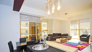 A modern kitchen with a central island, a dining area with chairs, a sofa, and a colorful rug. - Orange Lux Apartments (Budva)