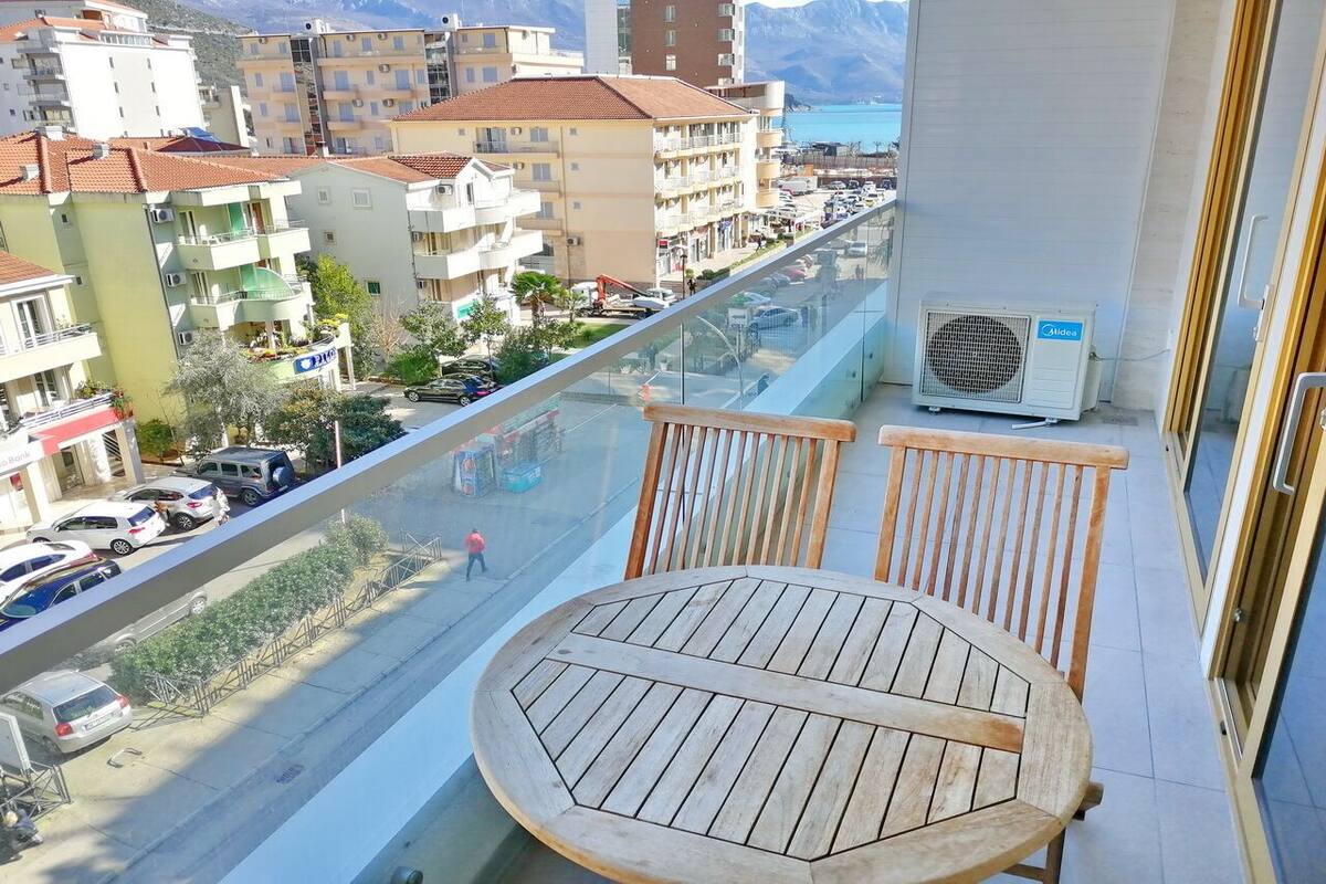 A balcony with a wooden table and chairs, overlooking a street with parked cars and buildings.