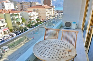 A balcony with a wooden table and chairs, overlooking a street with parked cars and buildings.