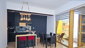 A modern kitchen with a dining area, featuring a built-in oven, microwave, and a hanging light fixture. - Orange Lux Apartments (Budva)