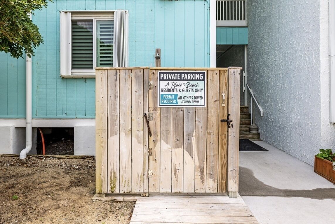 A wooden gate with a sign indicating private parking for residents and guests only, with a permit required.