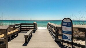 Ein hölzerner Steg führt zu einem Strand mit einem Schild.