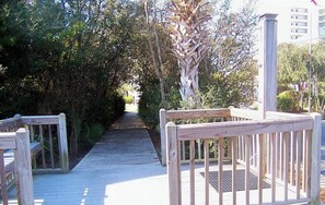 Stroll along the winding boardwalk through lush surroundings, bordered by a simple railing and a metal gate.