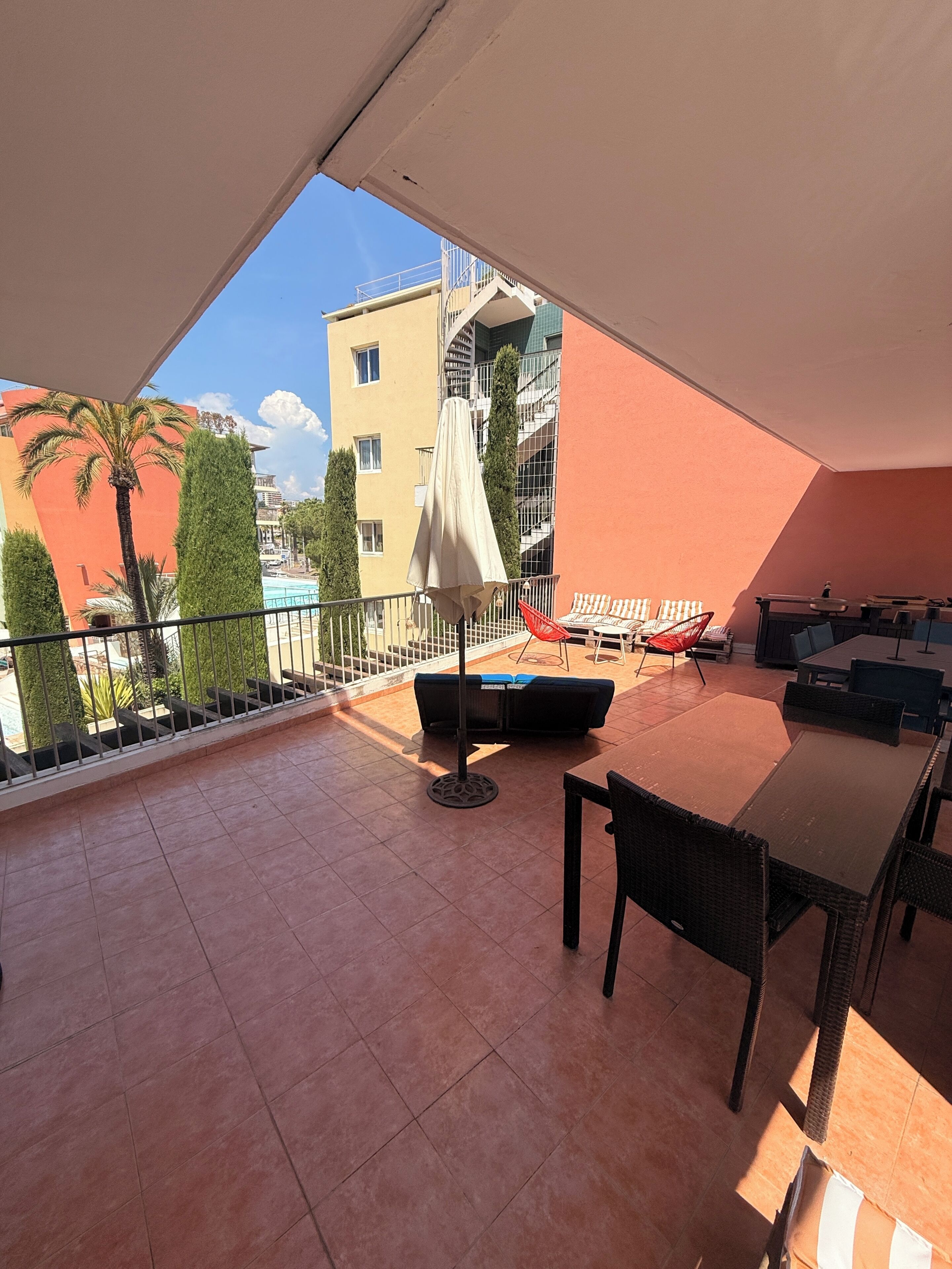 A balcony with a table, chairs, and a sun umbrella.
