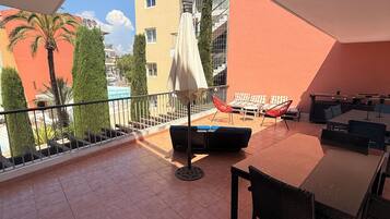 A balcony with a table, chairs, and a sun umbrella.