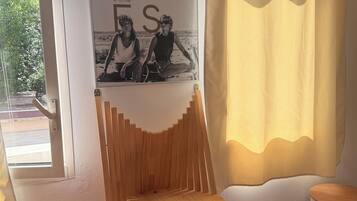 A room with a poster of the Cannes Film Festival, a window with a view of greenery, and a wooden shelf.