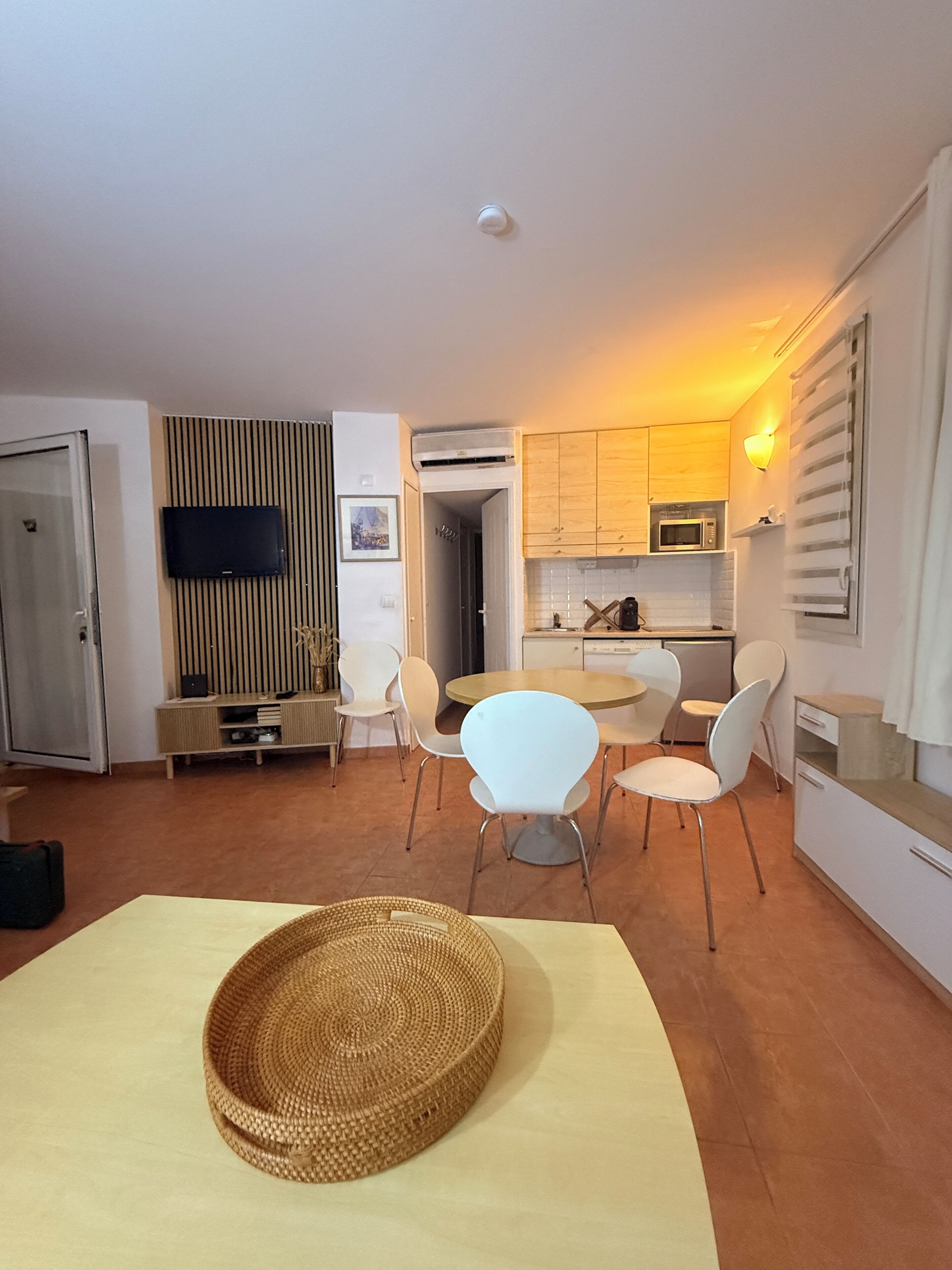 A compact living space with a dining area, kitchenette, and a television mounted on the wall.