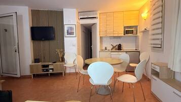 A compact living space with a dining area, kitchenette, and a television mounted on the wall.
