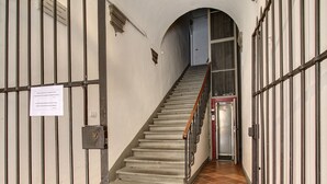 Een trap met metalen leuningen en een betegelde vloer, die naar een lift leidt.