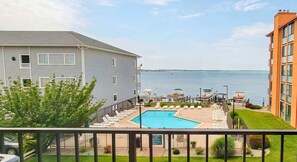 A pool area with lounge chairs, a view of the water, and a building with a grey facade. - 3BR Bayfront Getaway – Sun & Shore (Ocean City)
