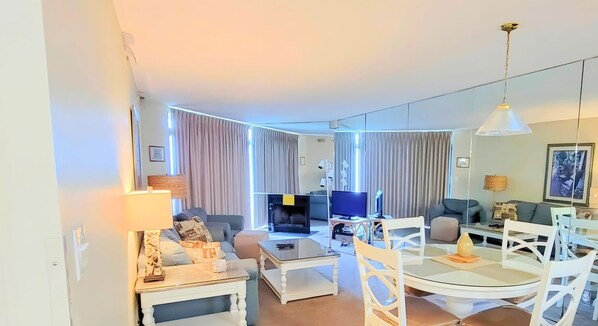 A modern living room with a sofa, a coffee table, a TV, and a dining area with chairs and a table. - 3BR Bayfront Getaway – Sun & Shore (Ocean City)
