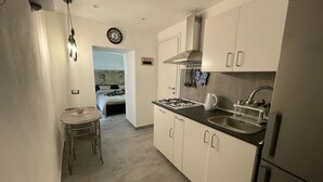 A compact kitchen with a dining area, a visible clock, and a bed in the adjacent room. - Tufoletto Apartment (Palermo)