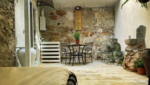 A stone-walled patio with a table and chairs, a potted plant, and a stone wall with plants. - Tufoletto Apartment (Palermo)