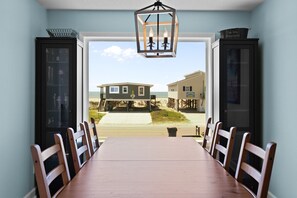A dining area with a view of beach houses through a large window. - Private pool, easy walk to the beach and a beautiful ocean views!  Seaside Shenanigans (Oak Island)