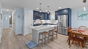 Una cocina moderna con armarios azul oscuro, una isla blanca, electrodomésticos de acero inoxidable y taburetes de bar de madera.