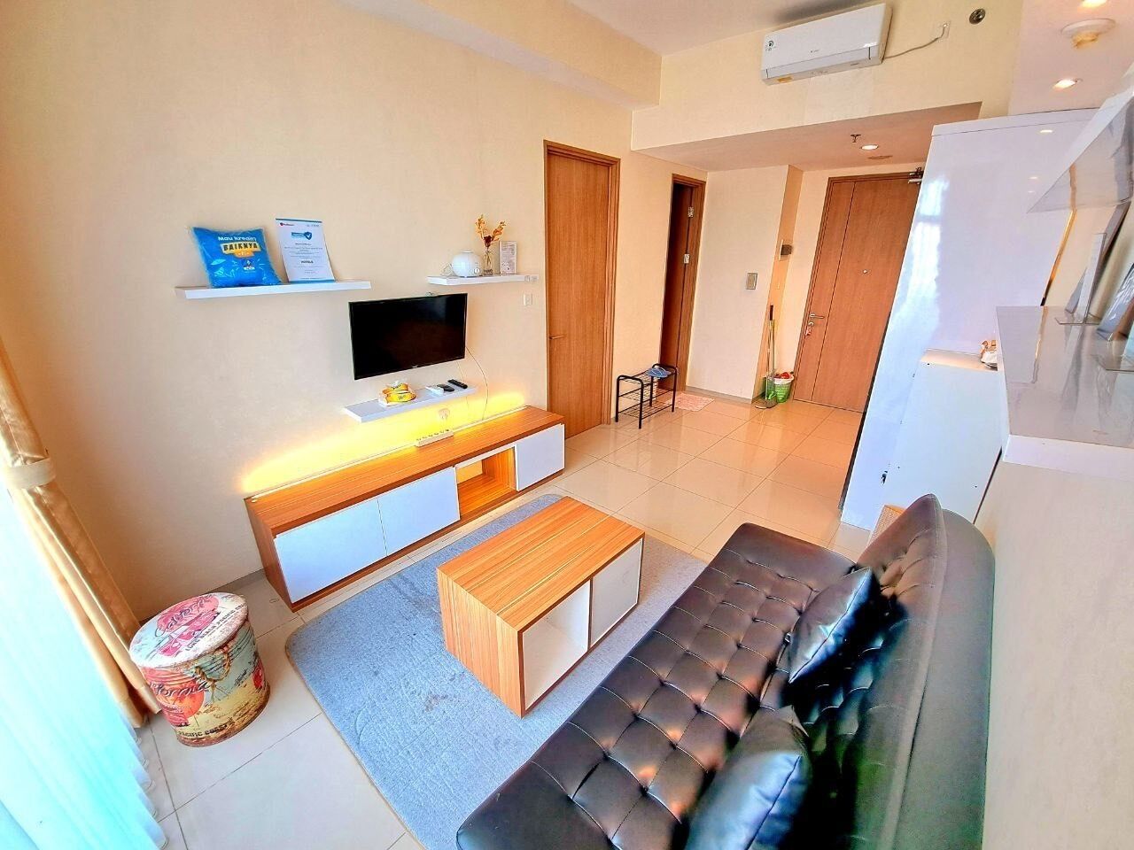 Een moderne woonkamer met een zwarte leren bank, een houten salontafel, een flatscreen televisie en een klein eethoekje met een tafel en stoelen.