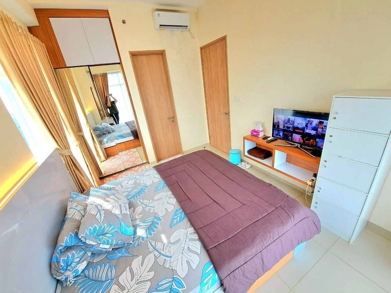 A hotel room with a bed, a television, a wardrobe, and a mirror.