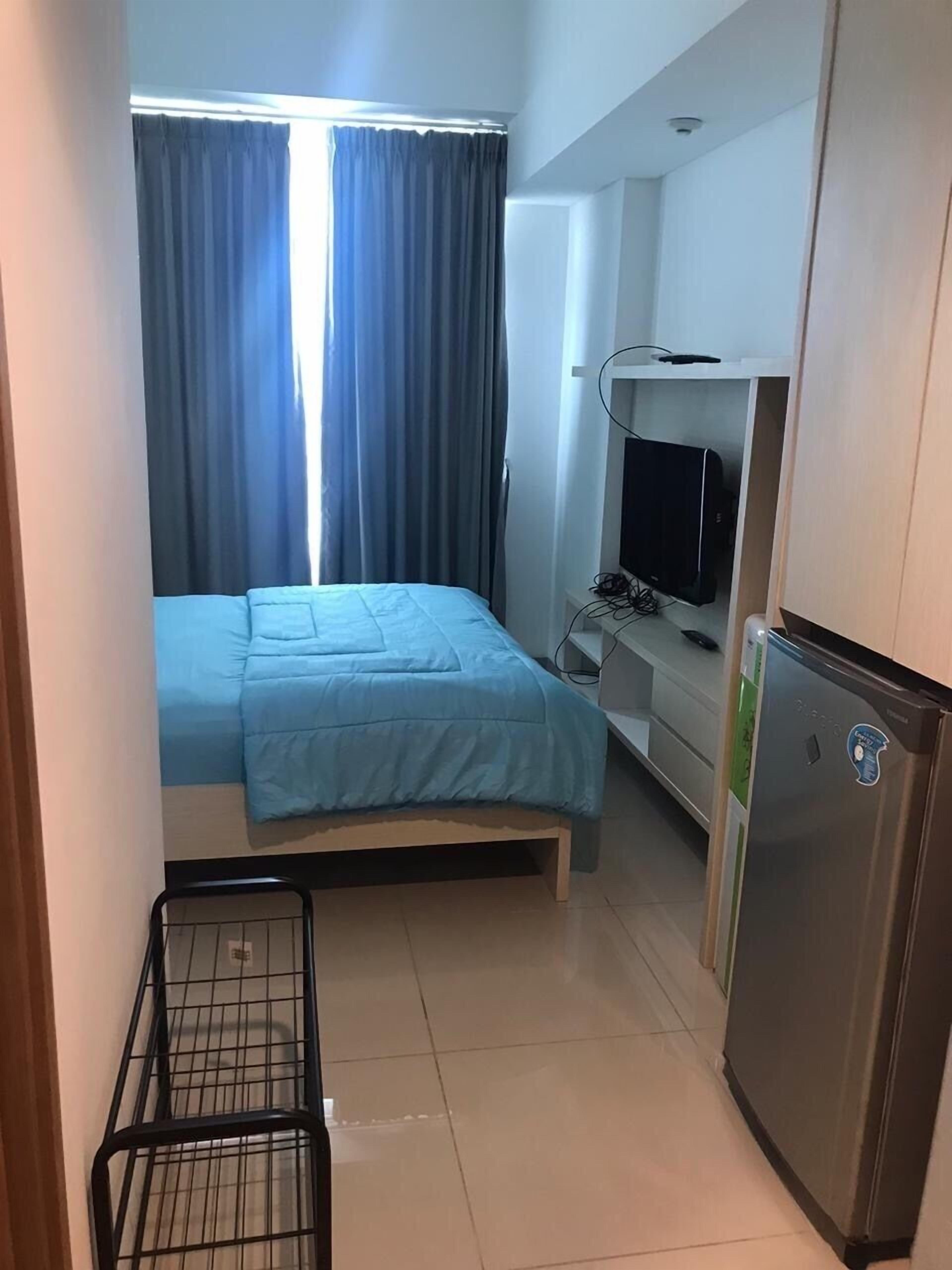 Una habitación pequeña con cama, escritorio con computadora, televisor y refrigerador.
