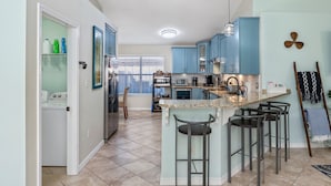 A modern kitchen with blue cabinets, a central island with bar stools, a built-in microwave, and a ceiling light fixture.