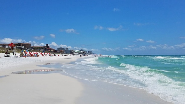 A beach with white sand, clear turquoise water, and a few umbrellas.