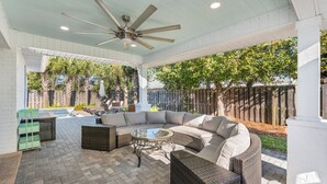 An outdoor patio with a curved sectional sofa, wicker furniture, a glass coffee table, and a ceiling fan.