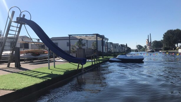 A canal with a blue slide, a boat, and houses along the water.
