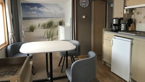 A compact kitchenette with a refrigerator, coffee maker, and stove. There is a dining area with a table and two chairs, and a view of the beach through the window.