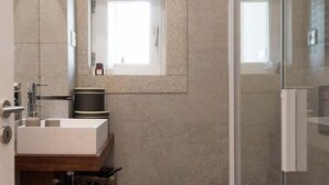 Ein modernes Badezimmer mit einer Duschkabine aus Glas, einem weißen Waschbecken mit Holzschrank und einem kleinen Fenster über dem Spiegel.