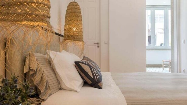 Ein Schlafzimmer mit einem großen Bett, einer Pendelleuchte und Blick ins Freie.