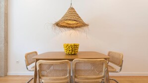 Ein Essbereich mit einem Holztisch, vier Korbstühlen, einer gewebten Pendelleuchte und einer Zitronenschale auf dem Tisch.