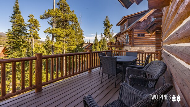 A wooden deck with wicker furniture, overlooking a forested area. - Pet Friendly Cabin| Hot tub, Deck & Trail (Big Sky)