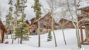 A log cabin with a stone exterior, surrounded by snow-covered ground and trees. - Pet Friendly Cabin| Hot tub, Deck & Trail (Big Sky)