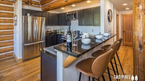 A modern kitchen with a stainless steel refrigerator, dark cabinets, a microwave, and a large island with bar stools. - Pet Friendly Cabin| Hot tub, Deck & Trail (Big Sky)