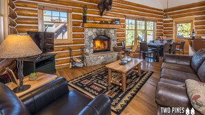 A log cabin interior with a stone fireplace, leather furniture, and a dining area. - Pet Friendly Cabin| Hot tub, Deck & Trail (Big Sky)