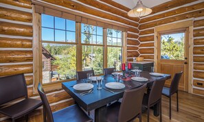 L’intérieur d’une cabane en rondins, avec une table à manger dressée pour six personnes, de grandes fenêtres et une vue sur l’extérieur.