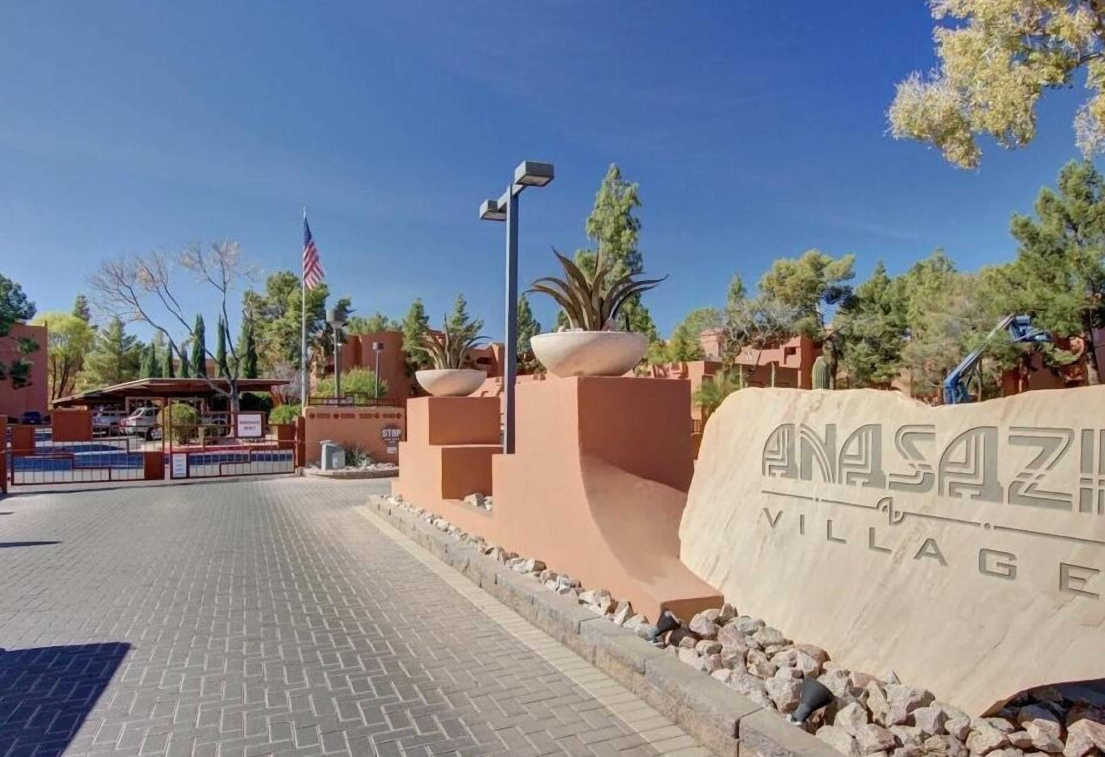 Een verharde oprijlaan met een bord waarop 'ANASAZI VILLAGE' staat en een Amerikaanse vlag.