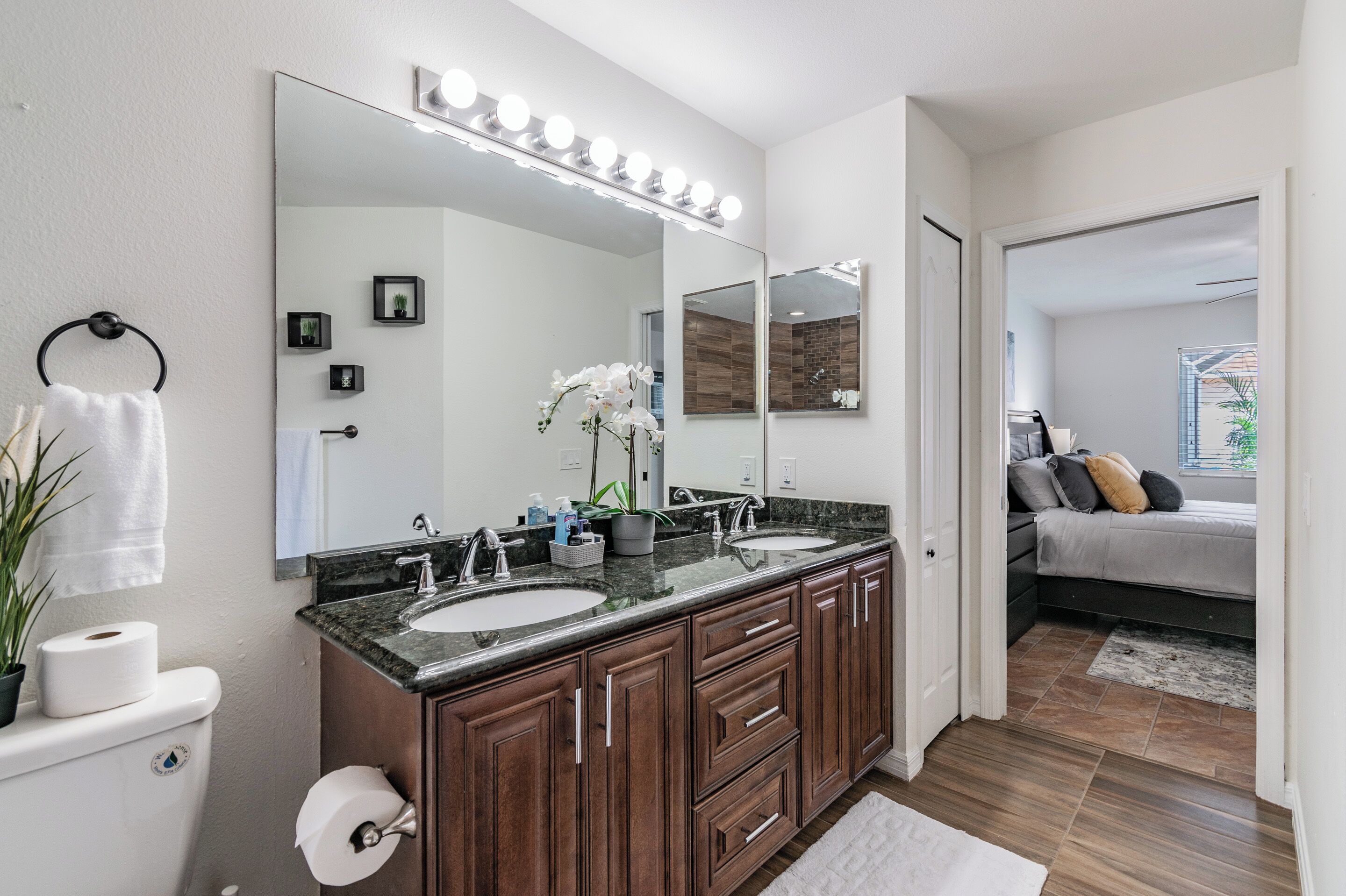 Un baño moderno con tocador doble, un espejo grande con luces y una zona de ducha visible.
