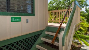 A staircase leading to a porch with a wooden railing, a sign reading "Plumeria", and a view of green foliage in the background. - Condo 500 Feet to the Ocean (Koloa)