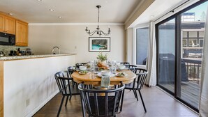 A modern kitchen with a dining area, featuring a large island, black chairs, and a chandelier.
