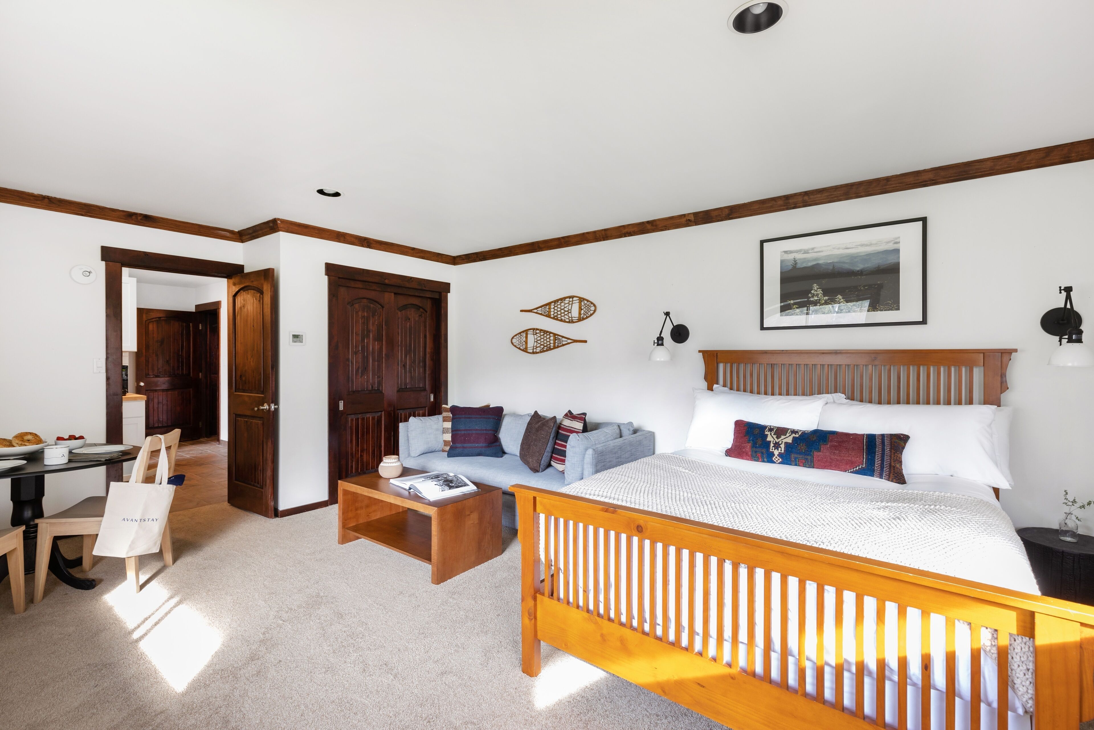 A bedroom with a wooden bed, a sofa, a coffee table, and a dining area with chairs and a table.