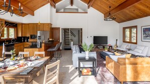 Un vaste espace de vie doté d’un haut plafond, de poutres apparentes, d’une table à manger dressée, d’un canapé et d’un téléviseur.
